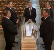 Porteurs funéraires en costume entourant un cercueil dans une église.